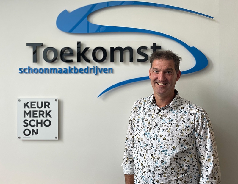 Tom Dissel à côté du logo de Toekomst Schoonmaakbedrijven